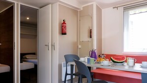 A compact hotel room with a kitchenette, a dining area with a bench, and a bed with a headboard.