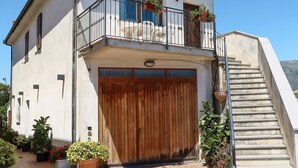 Una casa de dos pisos con un garaje de madera, un balcón con plantas en macetas y una escalera que conduce al piso superior.