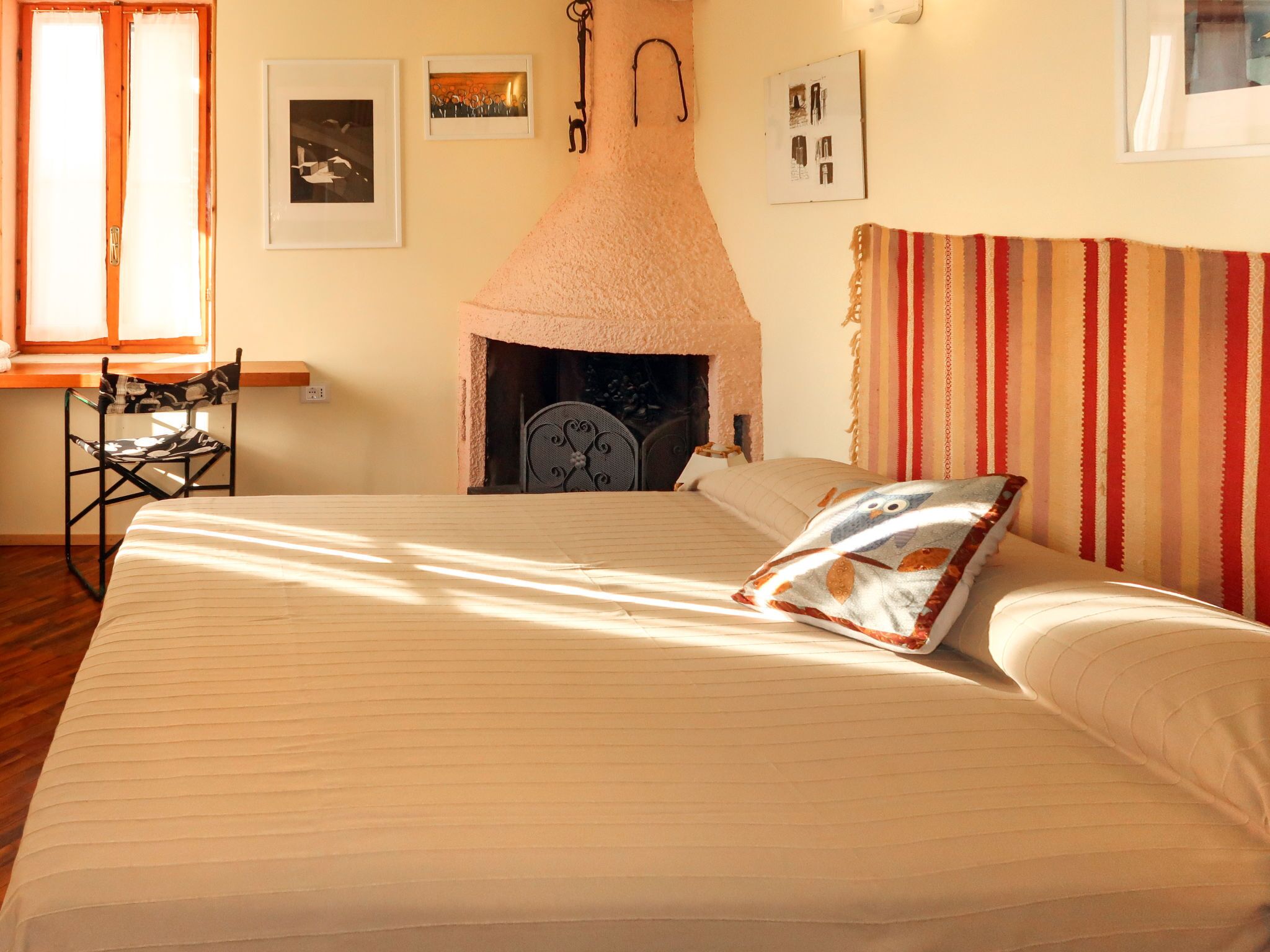 A bedroom with a bed, a fireplace, a window, and a chair.