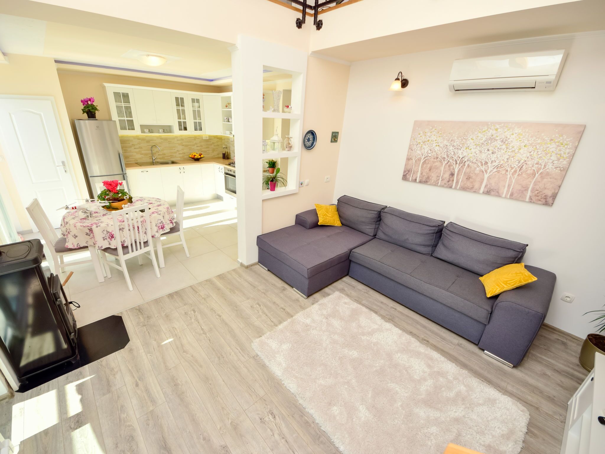 A modern living room with a grey sectional sofa, a dining table with chairs, and a kitchen in the background.