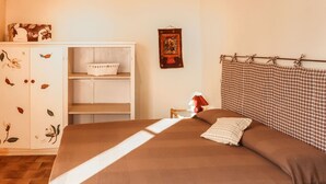 Une chambre avec un grand lit, une armoire à motifs floraux, une petite table avec une lampe et une décoration murale.