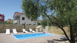 A swimming pool with lounge chairs, a stone wall, and a tree.