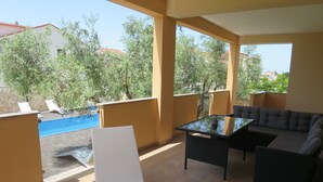 A balcony with a pool, outdoor furniture, and a view of trees and buildings.
