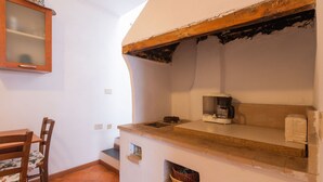 A kitchen with a coffee maker, a wooden cabinet with a glass door, a chair, and a tiled floor.