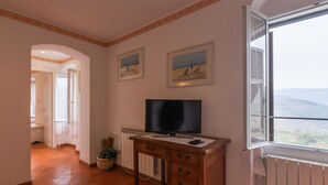 A room with a wooden desk, a television, and a window with a view of the landscape.
