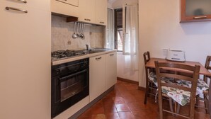 A compact kitchen with white cabinets, a gas stove, an oven, and a dining area with a table and chairs.