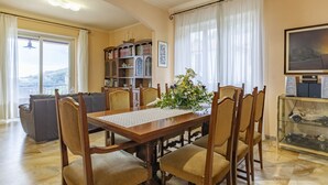 A dining area with a wooden table, six chairs, a vase of flowers, a bookshelf, and a painting on the wall.