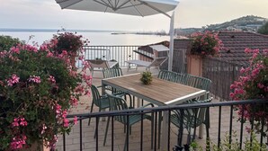 A terrace with a table and chairs, a white umbrella, and a view of the sea.
