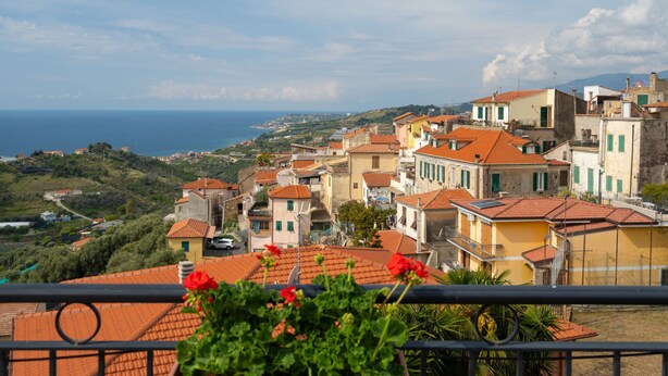 A coastal town with terracotta-roofed buildings, a clear view of the sea, and a balcony with red flowers. - Toni (TZR240) by Interhome (Terzorio)