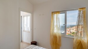 A bedroom with a bed, a window with curtains, a view of a cityscape, and a door leading to another room. - Toni (TZR240) by Interhome (Terzorio)