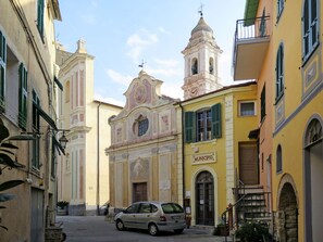 Uma rua estreita com edifícios históricos, uma igreja com um campanário e um carro estacionado.