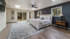 A bedroom with a bed, a ceiling fan, a nightstand, a lamp, and a large window. - Charming Modern A-frame Chalet with Hot Tub--8 min walk to Country Club (Angel Fire)