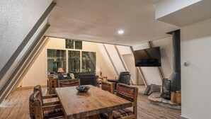 A cozy loft-style room with a wooden dining table, chairs, and a large TV. - Charming Modern A-frame Chalet with Hot Tub--8 min walk to Country Club (Angel Fire)