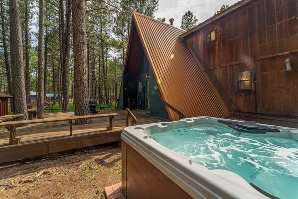 A wooden cabin with a hot tub, surrounded by tall trees. - Charming Modern A-frame Chalet with Hot Tub--8 min walk to Country Club (Angel Fire)