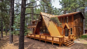 A cabin with a wooden exterior, a deck, and a staircase leading to the entrance. - Charming Modern A-frame Chalet with Hot Tub--8 min walk to Country Club (Angel Fire)