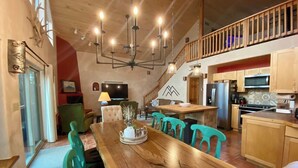 A spacious dining area with a wooden table and teal chairs, a kitchen with wooden cabinets, and a staircase leading to an upper level. - Spacious Cabin-6 min to AF Resort, min to hiking,biking,restaurants,grocerystore (Angel Fire)