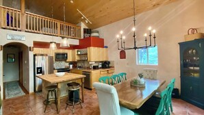 A spacious kitchen with wooden cabinets, a central island, and a dining area with teal chairs. - Spacious Cabin-6 min to AF Resort, min to hiking,biking,restaurants,grocerystore (Angel Fire)