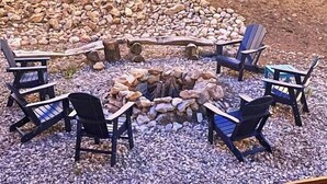 An outdoor seating area with a circular fire pit surrounded by Adirondack chairs, set on a gravel surface with string lights overhead. - Spacious Cabin-6 min to AF Resort, min to hiking,biking,restaurants,grocerystore (Angel Fire)