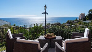 A terrace with wicker furniture, a table with a centerpiece, and a view of the sea.