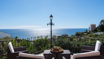 Una terrazza con mobili in vimini, un tavolo con un elemento decorativo e vista sul mare.