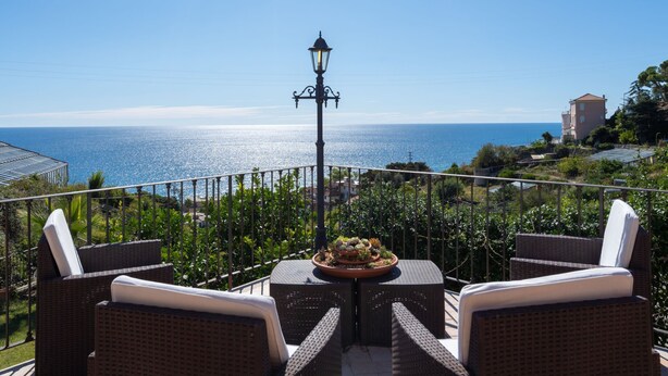Una terraza con mobiliario de mimbre y una mesa con una planta, con vistas a la costa.
