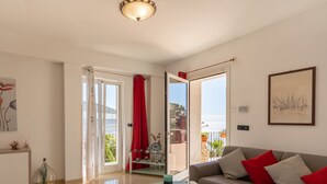 Una sala de estar moderna con una mesa de centro de vidrio, un sofá gris con cojines rojos, un cuadro en la pared y un balcón con cortinas rojas.
