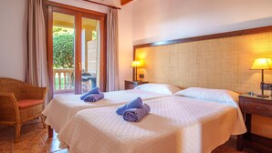 Une chambre d’hôtel avec deux lits, une chaise en osier, un balcon avec des rideaux et un plafond en bois.