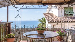 An outdoor patio with a round table and chairs, surrounded by potted plants and striped cushions. - Villa Ginestra by Interhome (Ventimiglia)
