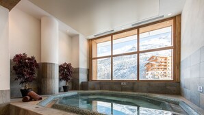 A spa area with a hot tub, potted plants, and a large window offering a mountain view. - Le Lodge des Neiges 5* by Interhome (Tignes)