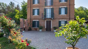 A two-story brick building with a central entrance, potted plants, and a cobblestone courtyard. - Marmorito by Interhome (Portacomaro)