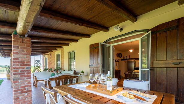 A covered outdoor dining area with a wooden table, chairs, and a brick pillar. - Marmorito by Interhome (Portacomaro)