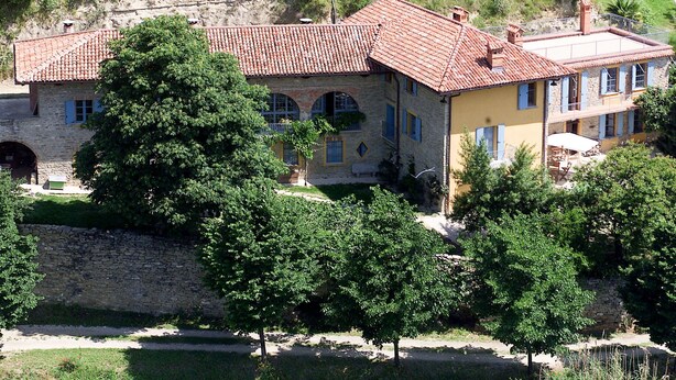 Una casa de pedra de dos pisos amb teules vermelles, un mur de pedra i una petita zona de jardí.