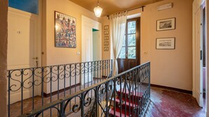 Una escala amb barana metàl·lica ornamentada, un aterri amb moqueta vermella i vista a una porta que condueix a una altra habitació.