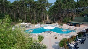 A pool area with lounge chairs and umbrellas, surrounded by trees.