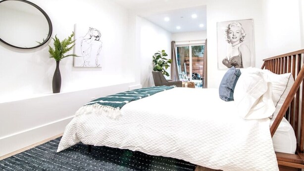A modern bedroom with a bed, a mirror, a plant, and artwork on the walls.