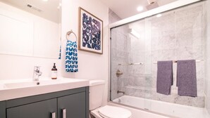 A modern bathroom with a white sink, dark cabinets, a toilet, and a glass-enclosed shower area.