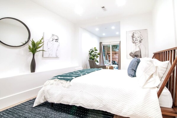 Un dormitorio moderno con una cama, un espejo, una planta y obras de arte en las paredes.