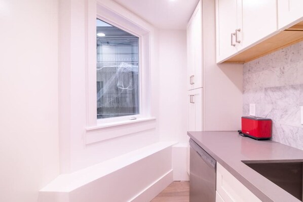 A narrow kitchen with white cabinetry, a window with frosted glass, and a red toaster on the counter.