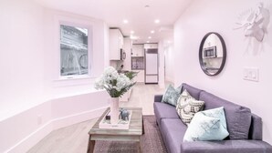 A modern living room with a sofa, a coffee table with a floral arrangement, and a view of a kitchen and dining area.
