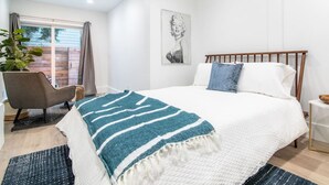 A bedroom with a bed, a chair, a window, and a plant.