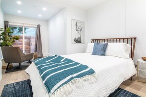 Un dormitorio con cama, una silla, un ventanal grande y una planta.