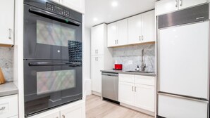 A modern kitchen with white cabinets, a stainless steel oven, a dishwasher, and a refrigerator.
