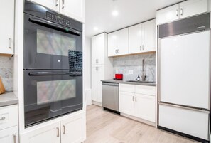 Una cocina moderna con armarios blancos, horno de acero inoxidable, lavavajillas y refrigerador.