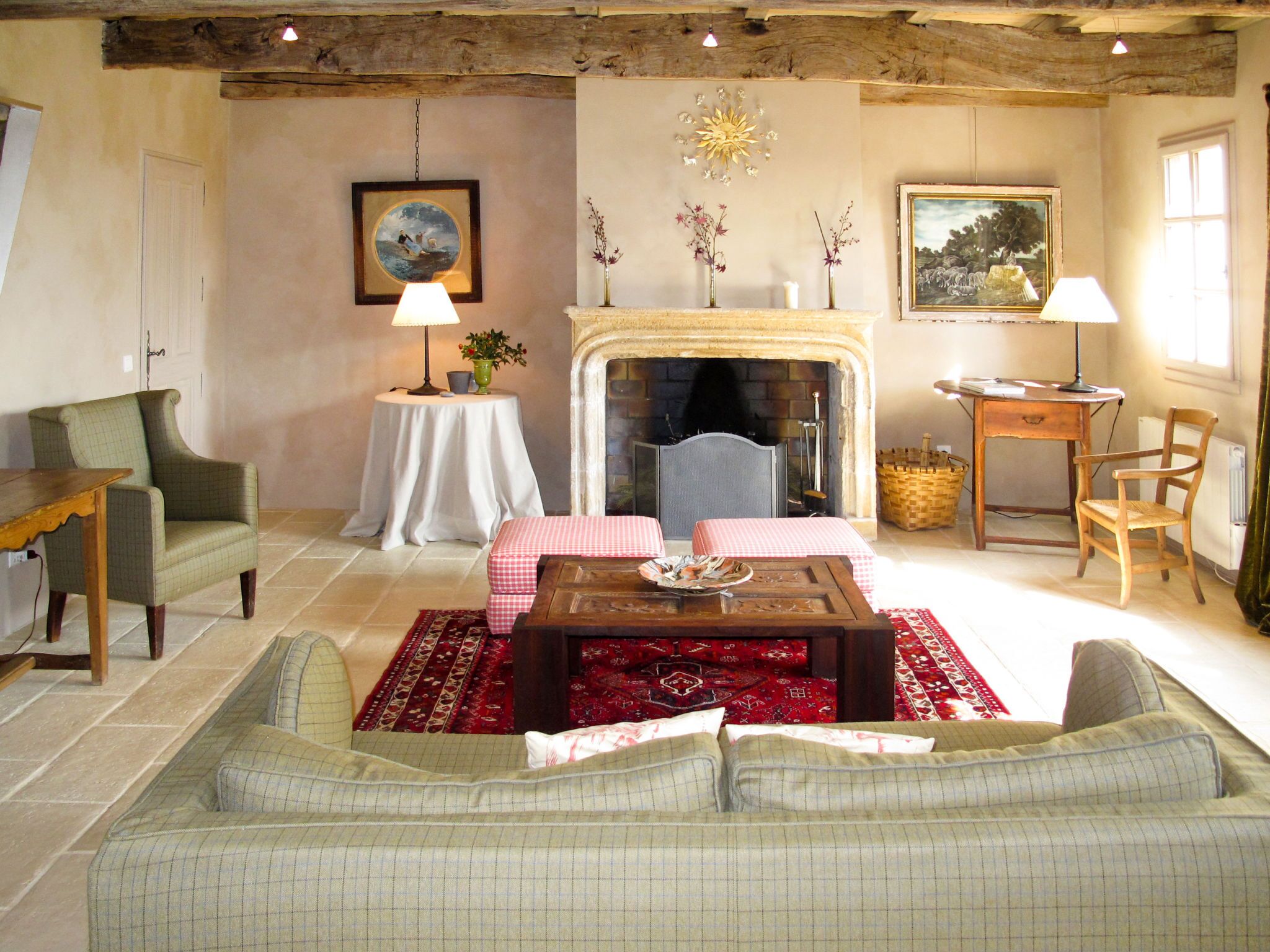 A cozy living room with a fireplace, a sofa, a dining table with a checkered tablecloth, and a small side table with a lamp.