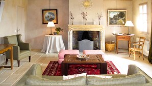 A cozy living room with a fireplace, a sofa, a dining table with a checkered tablecloth, and a small side table with a lamp. - Le Collet des Redons by Interhome (Lorgues)