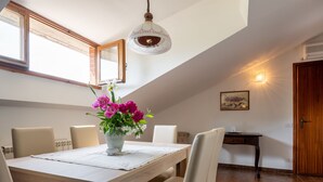 A dining area with a wooden table, white chairs, a vase of flowers, and a pendant light. - Ca' D'Gnese by Interhome (Castagnole Lanze)