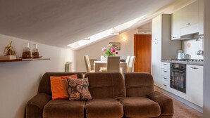 A cozy living room with a brown sofa, a dining table with chairs, and a kitchen area with cabinets and appliances. - Ca' D'Gnese by Interhome (Castagnole Lanze)