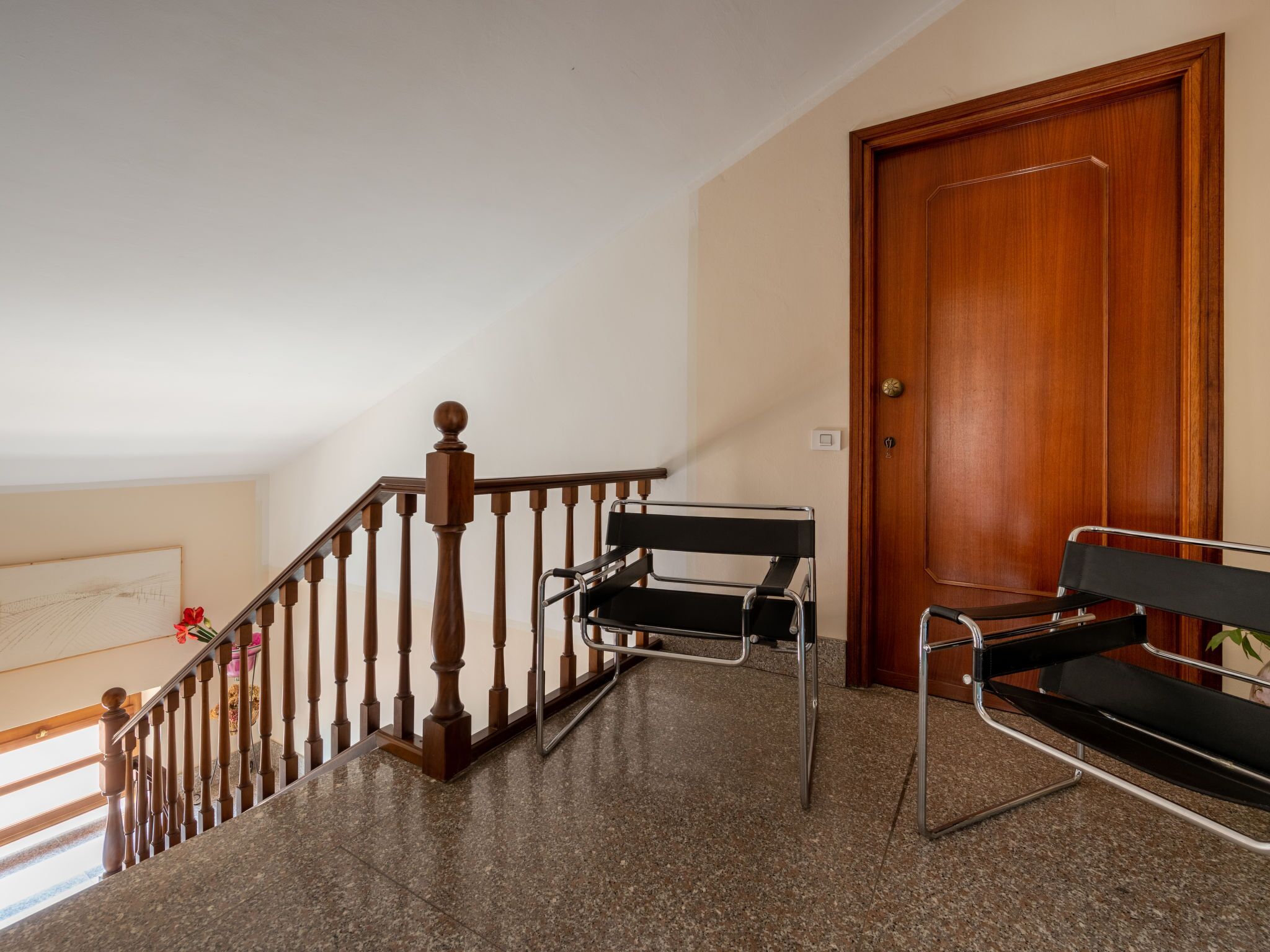 Un escalier avec des balustrades en bois, une chaise en métal noir et une porte en bois.