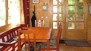 A wooden interior with a dining table, chairs, and benches. There are windows and doors with glass panes. - Vacation home Hajnal by Interhome (Balatonfenyves)