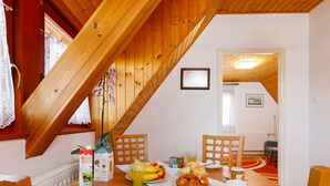 Een ontbijttafel gedekt met croissants, bananen, sap en koffie in een kamer met houten balken en uitzicht op een andere kamer.